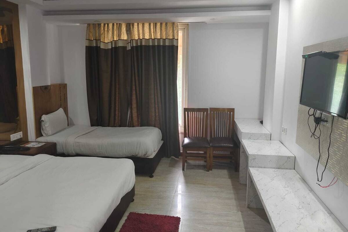 A hotel room with two beds, a desk, a chair, a TV mounted on the wall, and a window with curtains.