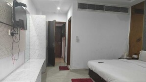 A bedroom with a bed, a TV mounted on the wall, a red rug, and a hallway leading to another room. - The Park Ambanc-New Delhi (New Delhi)