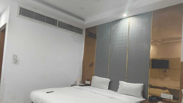 A double bed with white linens, a red rug, a wooden nightstand with a phone and a lamp, and a wall-mounted TV. - The Park Ambanc-New Delhi (New Delhi)