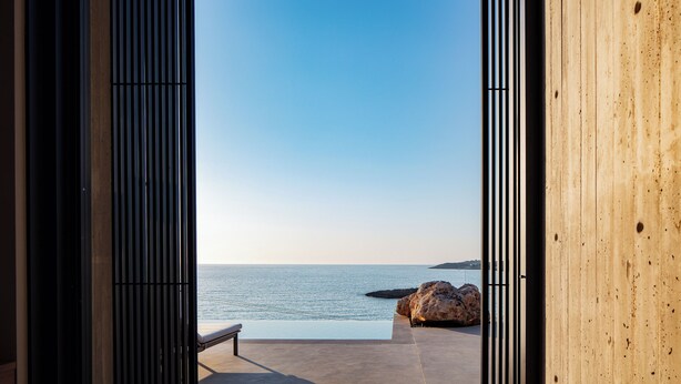 A view from a room with a large window overlooking a calm sea and a rocky outcrop. - Coastal Villa Defined by Detail & Sleek Simplicity by etouri (Chania)