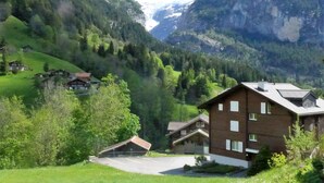 A mountain village with traditional chalet-style buildings, a parking area, and a view of snow-capped mountains. - Chalet Mettli by Interhome (Grindelwald)