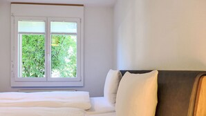 A bedroom with a bed, white bedding, a window with a view of greenery, and a dark headboard. - Chalet Mettli by Interhome (Grindelwald)