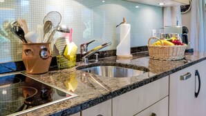 A kitchen with a granite countertop, stainless steel sink, and modern cabinetry. There are utensils in a brown pot and a basket with fruits on the counter. - Chalet Mettli by Interhome (Grindelwald)