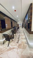 A hotel lobby with a long reception desk, several wooden chairs, and a marble floor.