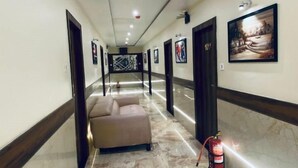 A hotel hallway with marble flooring, a sofa, framed artwork on the walls, and a fire extinguisher. - Hotel BKC Prime  (Mumbai)
