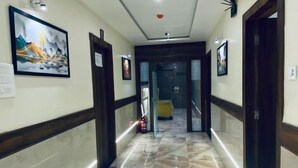 A hotel hallway with marble flooring, framed artwork on the walls, and doors leading to rooms. - Hotel BKC Prime  (Mumbai)