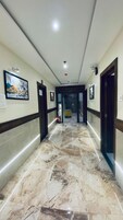 A hotel hallway with marble flooring, framed artwork on the walls, and doors leading to rooms.