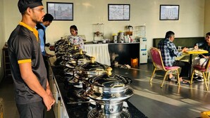A buffet setup with multiple serving stations, a counter with food items, and a seating area with tables and chairs. - Hotel BKC Prime  (Mumbai)