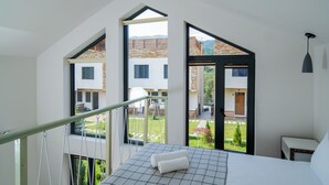 A bedroom with a large bed, a view of a garden, and a balcony with a railing. - Taniqinn Dilijan Cottages  (Dilijan)