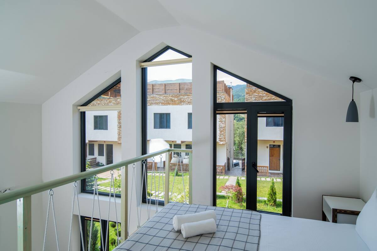 Ein Schlafzimmer mit einem großen Bett, Blick auf einen Garten und einem Balkon mit Geländer.
