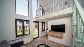 A spacious living area with a high ceiling, large windows, a balcony, and a flat-screen TV mounted on the wall. - Taniqinn Dilijan Cottages  (Dilijan)