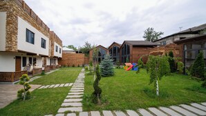 A courtyard with a stone pathway, wooden fences, and a small play area with a slide. - Taniqinn Dilijan Cottages  (Dilijan)