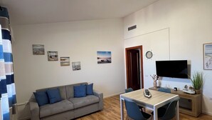 Una sala de estar moderna con un sofá gris, una mesa de comedor de madera y un televisor de pantalla plana montado en la pared.