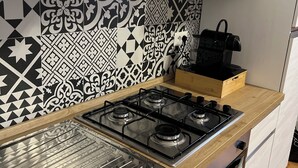 Cocina con estufa a gas, horno y microondas. Cuenta con una encimera de madera y salpicadero con baldosas blanco y negro.