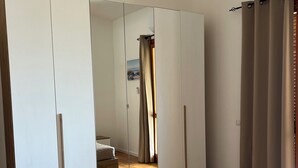 Un dormitorio con un espejo grande, una cama con colcha color crema y suelo de madera.