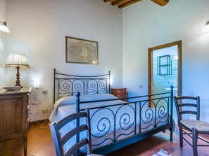 A bedroom with a bed, a nightstand, a lamp, a chair, and a window.