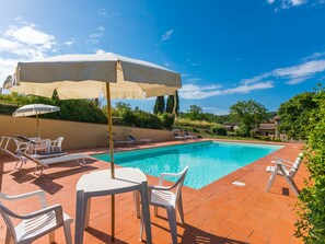 A swimming pool with lounge chairs and umbrellas, surrounded by a brick patio and greenery.