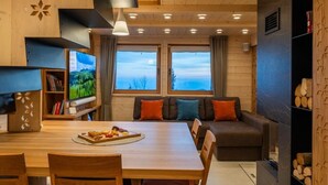 A cozy cabin interior with a dining area, sofa, and a television on a wooden shelf.