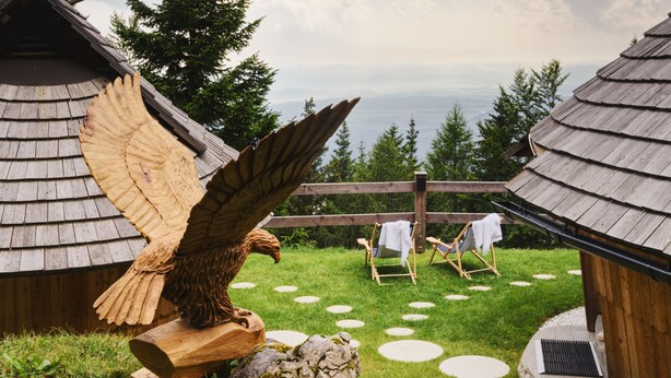 A rustic lodge with wooden cabins, a large wooden eagle sculpture, and a scenic view of trees and mountains.