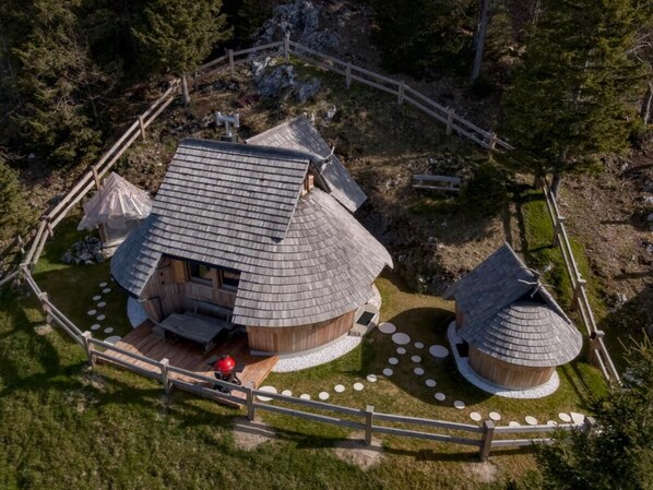 Una estructura circular de madera con techo de paja, rodeada por una valla de madera y senderos de piedra.