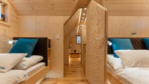 A wooden cabin with two bunk beds, each with a pillow and a small bedside table.