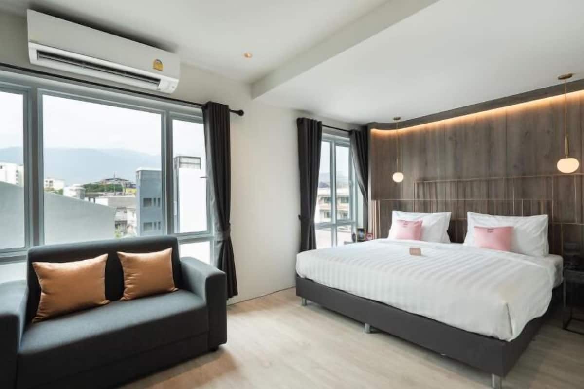 Una habitació d'hotel moderna amb un llit gran, un sofà i vista a la ciutat a través de grans finestres.