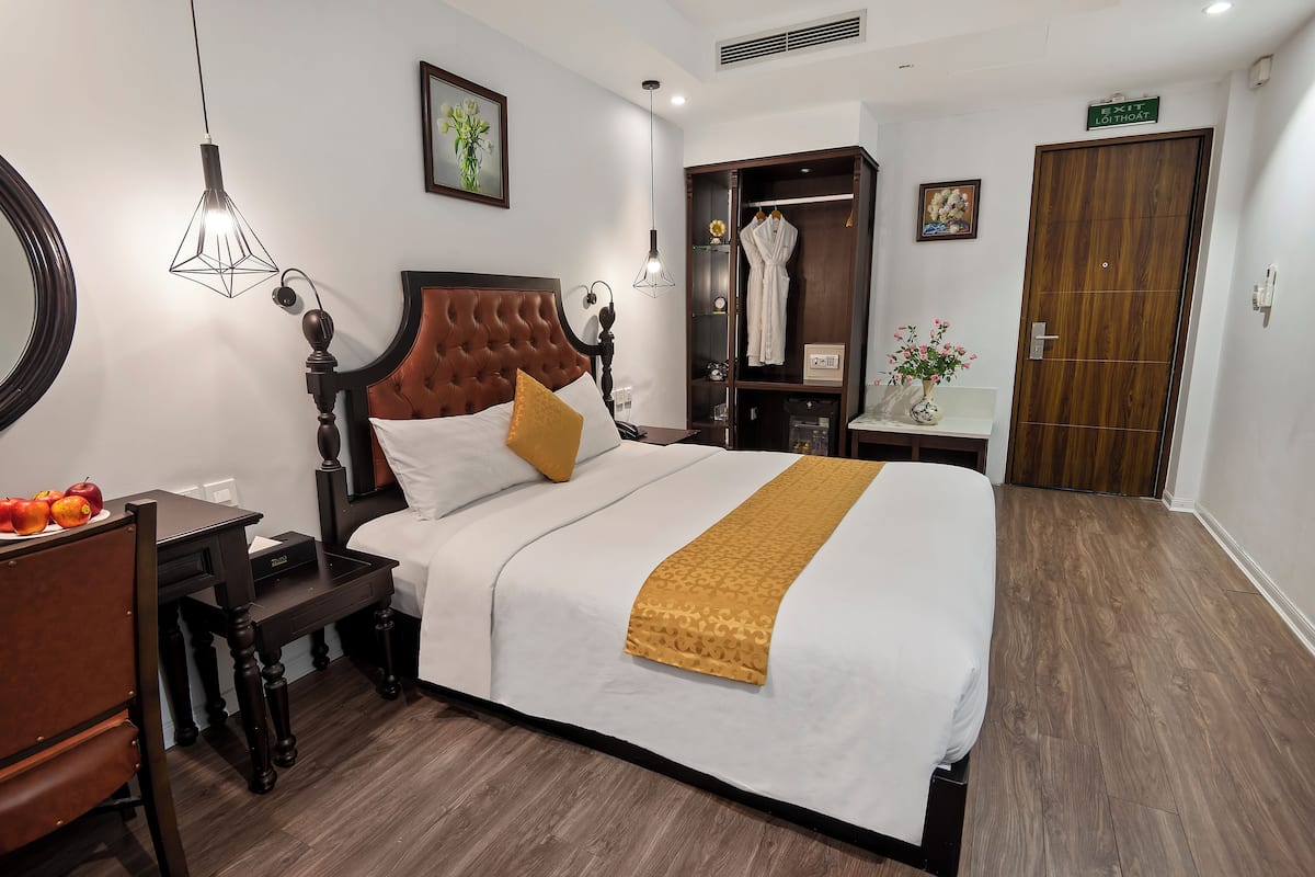A neatly arranged hotel room with a large bed, a wooden wardrobe, a bedside table with a lamp, and a mirror on the wall.