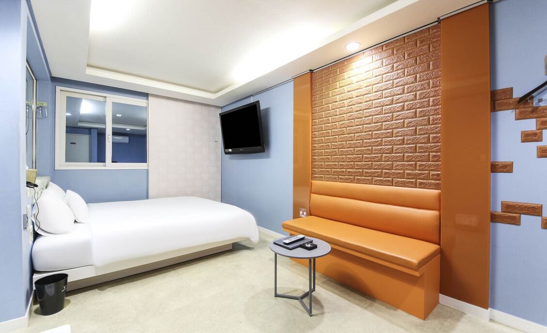 A modern hotel room with a bed, a small table, a TV, and a brick-patterned wall.