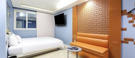 A modern hotel room with a bed, a small table, a TV, and a brick-patterned wall.