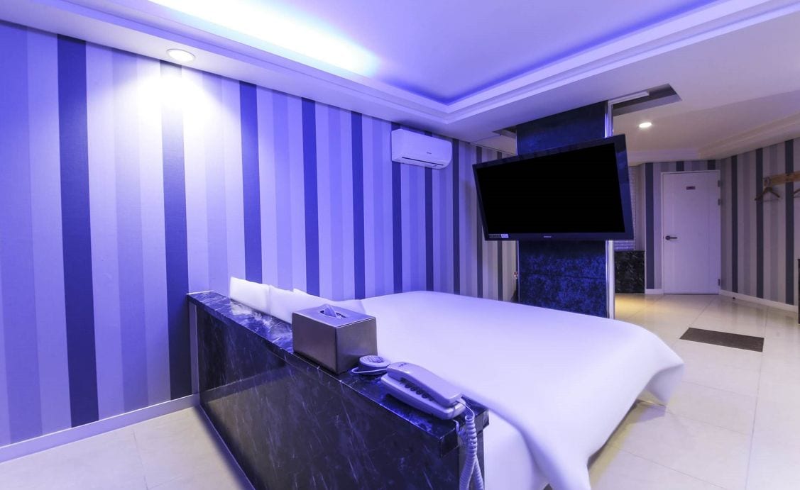 Quarto de hotel com uma cama grande, televisão de tela plana na parede, escrivaninha com telefone e minibar.