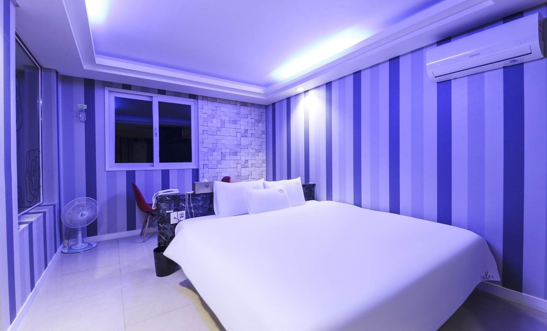 A bedroom with a bed, a window, a fan, and striped walls.