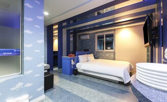 Una habitación de hotel con cama, escritorio, silla, televisor y baño con lavamanos y espejo.