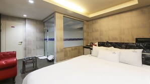 Une chambre d’hôtel avec un grand lit, une chaise rouge, une petite table et un miroir au mur.