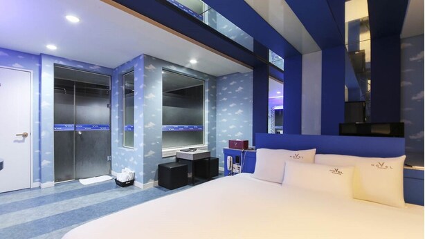 Une chambre d’hôtel moderne dotée d’un grand lit, d’une coiffeuse avec miroir, d’un dressing et d ’une salle de bain avec douche et toilettes.