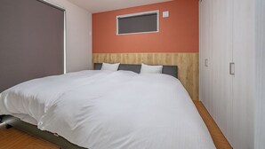 Una cama bien tendida en una habitación con cabecera de madera, una ventana pequeña y un armario blanco.