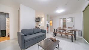 Un apartamento moderno con un sofá gris, una mesa de comedor de madera con sillas, una zona de cocina y una pequeña mesa de centro con un control remoto.