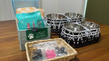 A dining table with pet amenities including a pet bed, bowls, and a basket with pet food and toys.