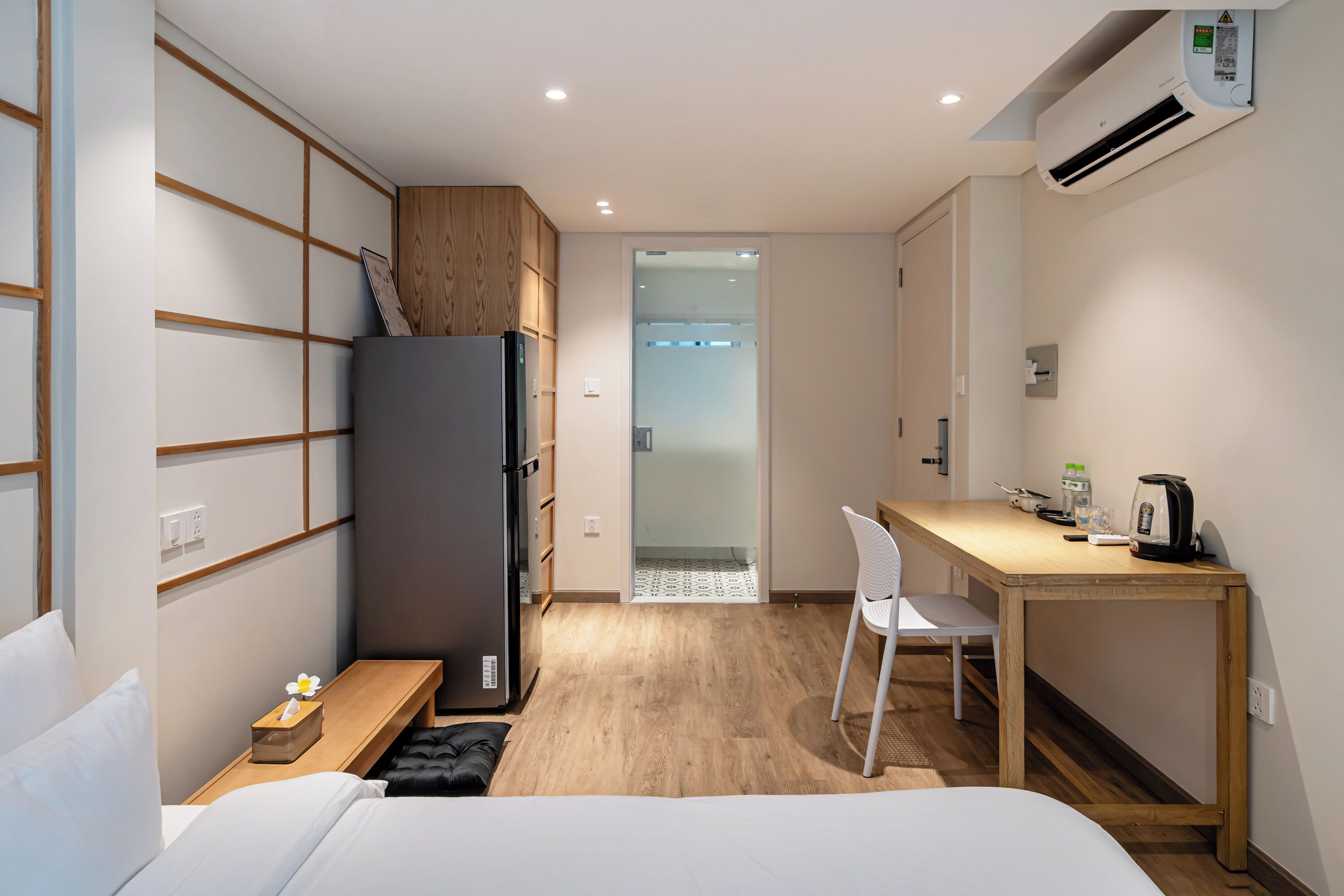 Habitación de hotel compacta con cama, escritorio, silla, refrigerador y pequeña zona de kitchenette.