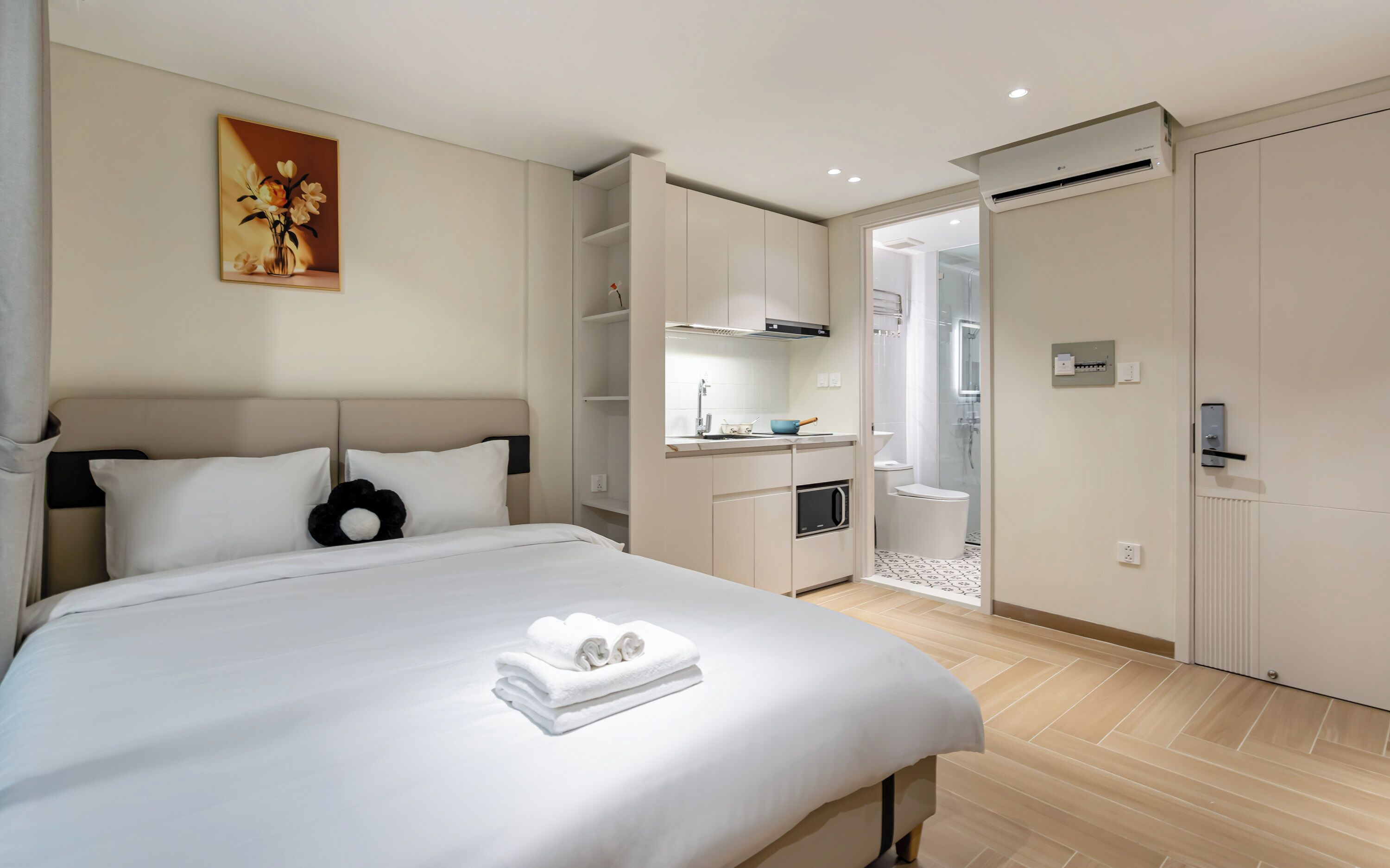 A hotel room with a bed, a small kitchenette, a bathroom, and a shower.