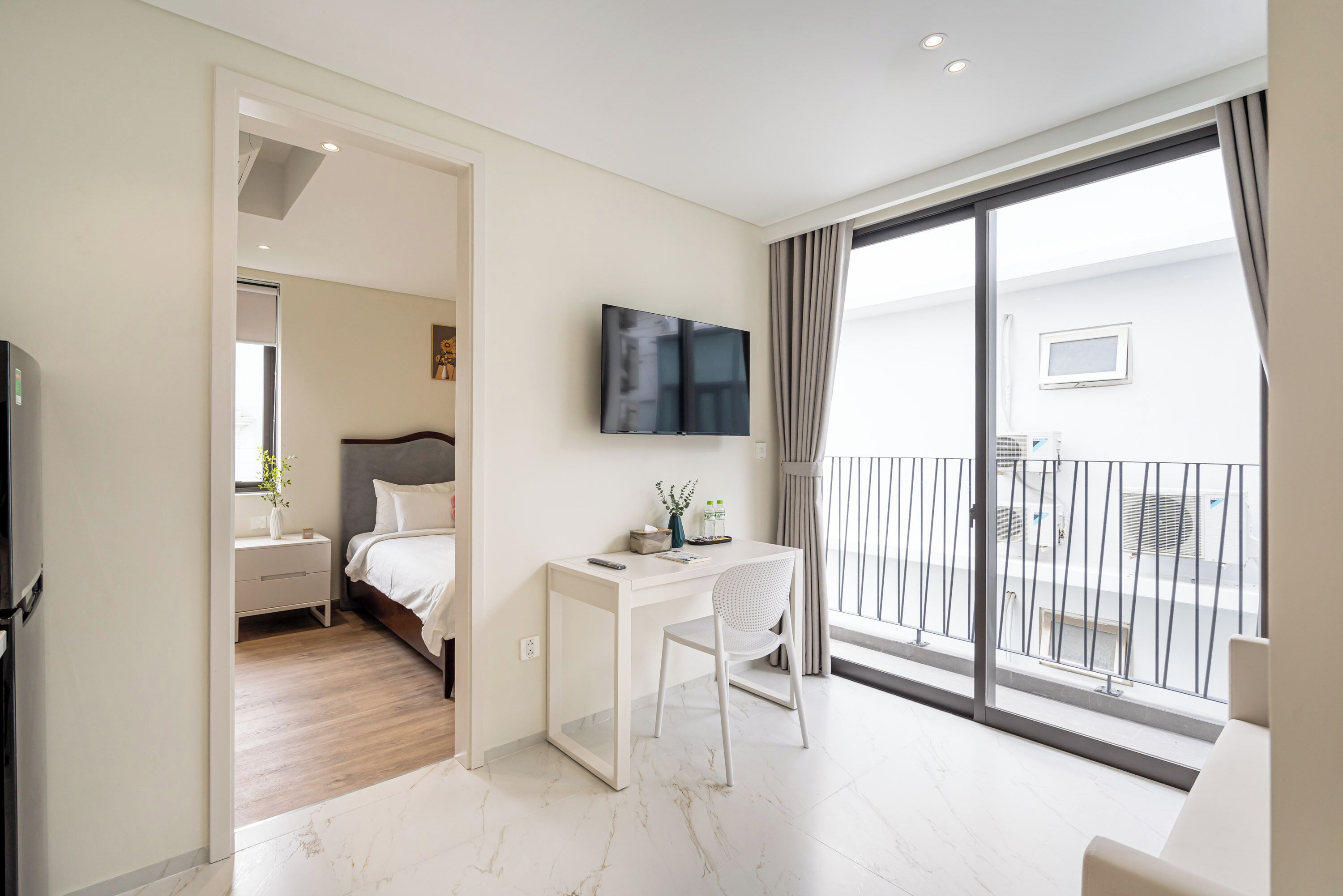 Habitació d'hotel moderna amb un llit, escriptori, cadira, televisió i un balcó amb barana.