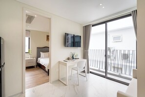 A modern hotel room with a bed, a desk, a chair, a TV, and a balcony with a railing. - The Royal Vista - Phu My Hung (Ho Chi Minh City)