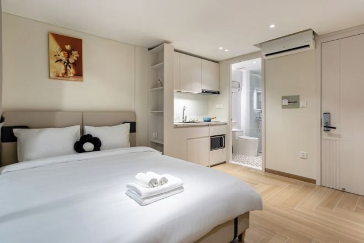 A modern hotel room with a large bed, a kitchenette, and a bathroom.