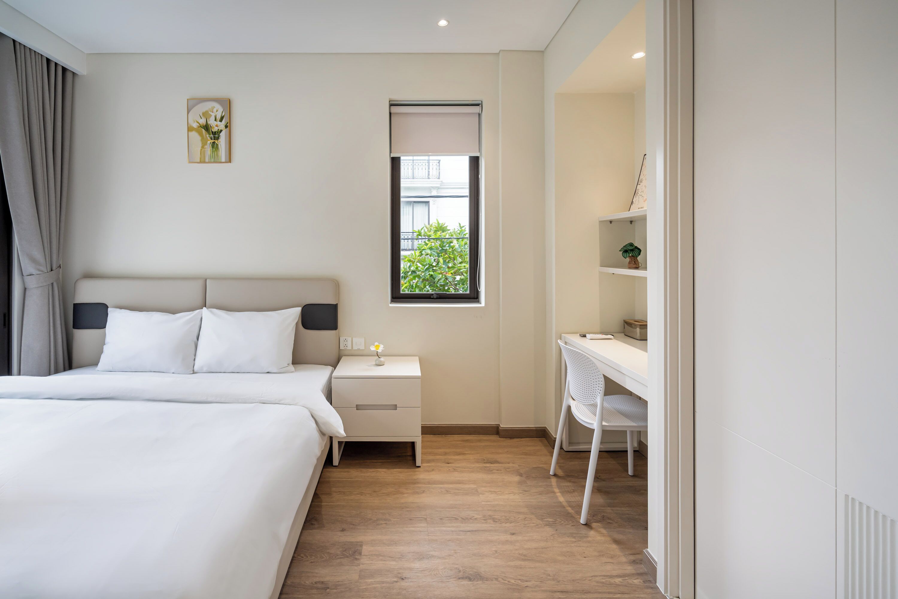 A modern hotel room with a large bed, a desk, and a window with a view of greenery.