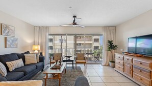 A living room with a sofa, chairs, a coffee table, a TV, and a balcony with a view.