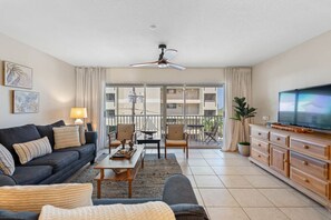 A living room with a sofa, chairs, a coffee table, a TV, and a balcony with a view.