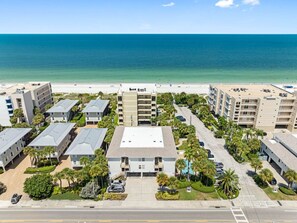 A multi-story hotel with a central courtyard, parking, and a beach view.