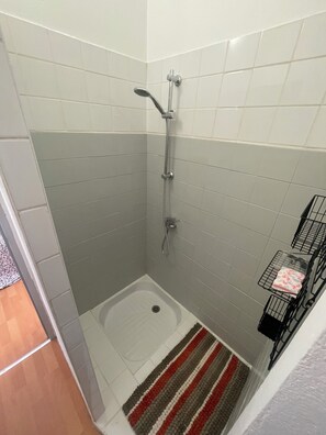 A small, tiled shower area with a showerhead, a handheld shower attachment, and a small rectangular sink. - Appartement Centre-ville (Uzès)