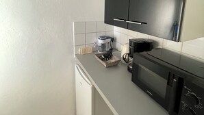 A compact kitchen with a white refrigerator, a black microwave, and a coffee maker on the counter. - Appartement Centre-ville (Uzès)