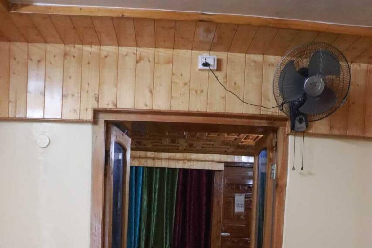 A wooden-paneled room with a bed, a fan, and a door leading to another room.