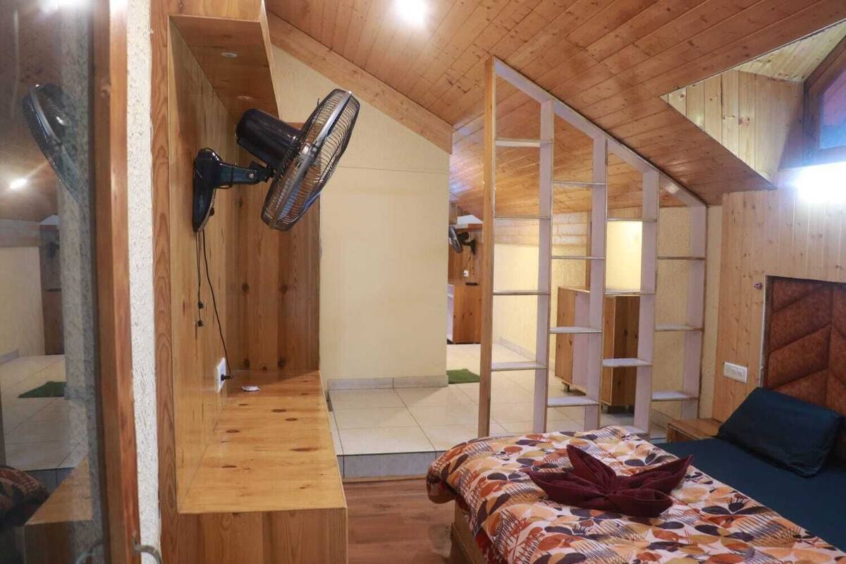 A wooden room with a bed, a standing fan, and a wooden shelf.